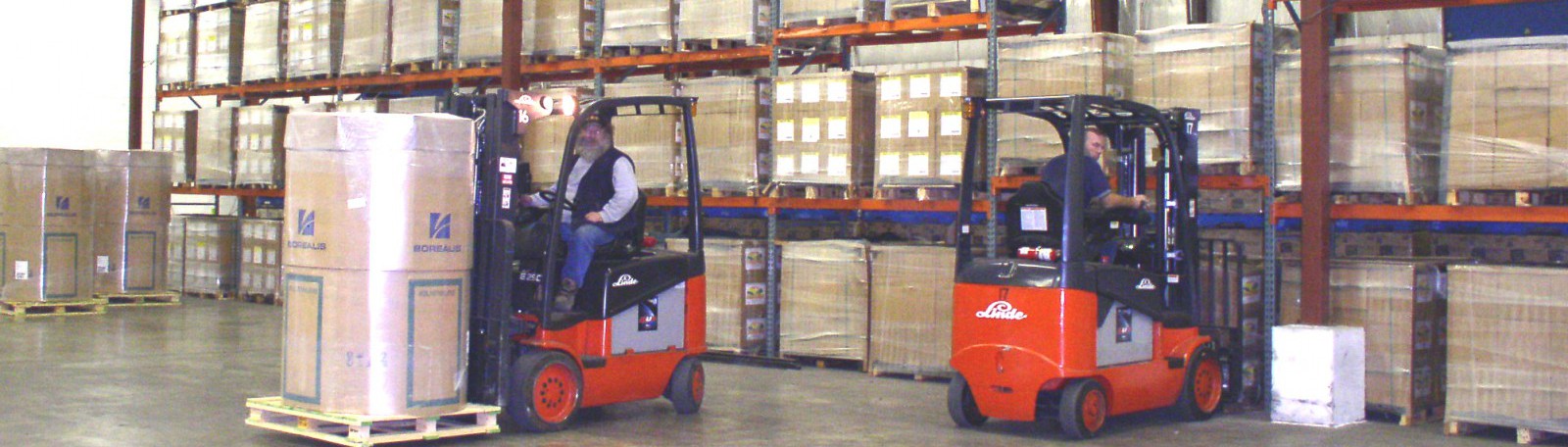 Two men on forklifts moving boxes off of shelves