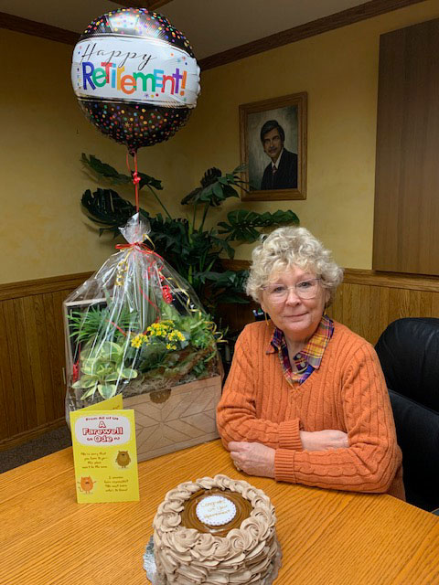 Jeannie sitting beside a plant gift basket, card, cake and balloon for her retirement.